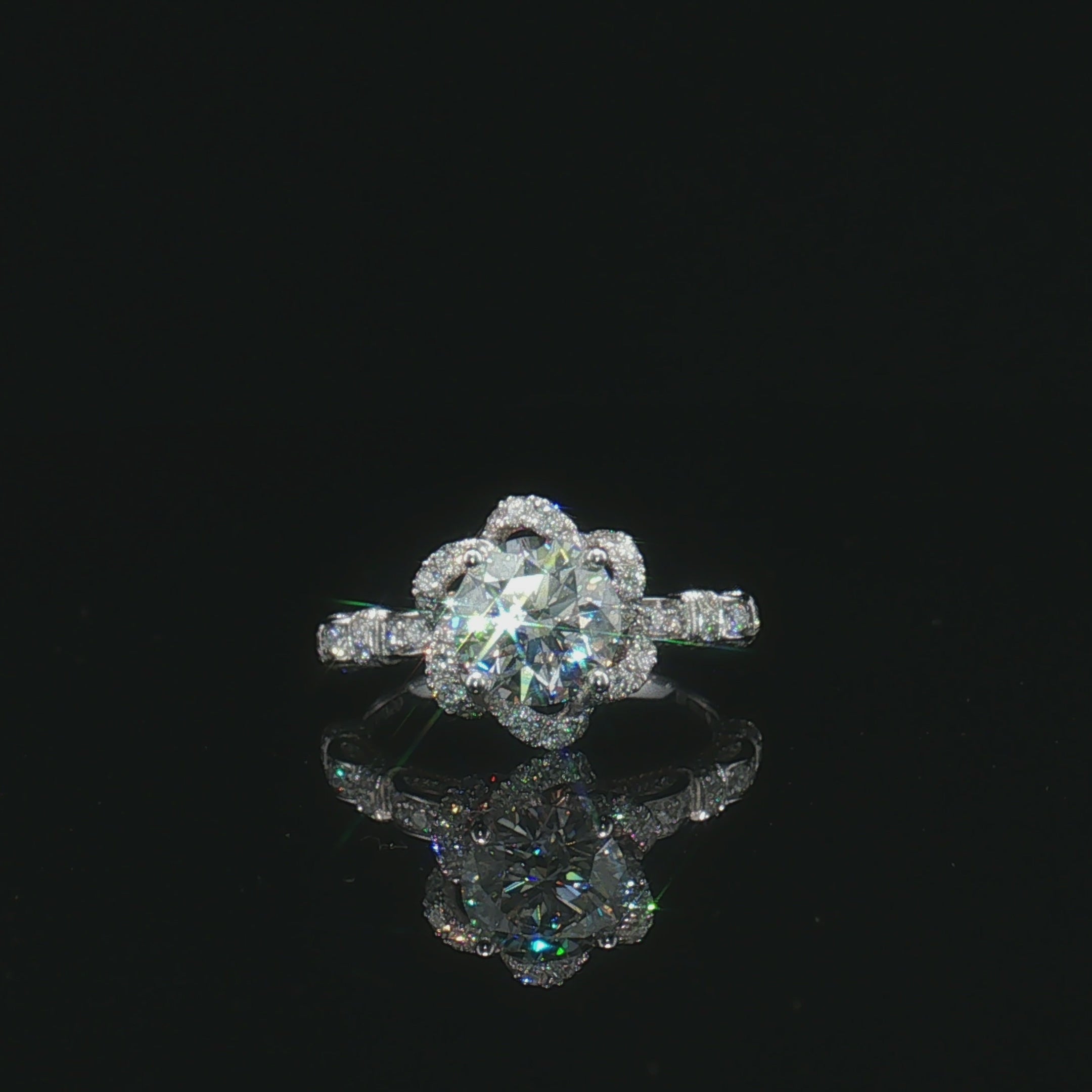 Round centre stone ring with a floral halo and geometric pavé shoulders on a black surface