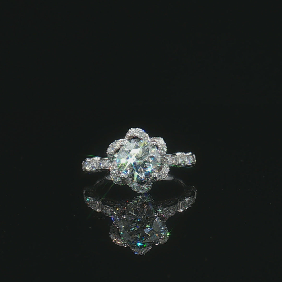 Round centre stone ring with a floral halo and geometric pavé shoulders on a black surface